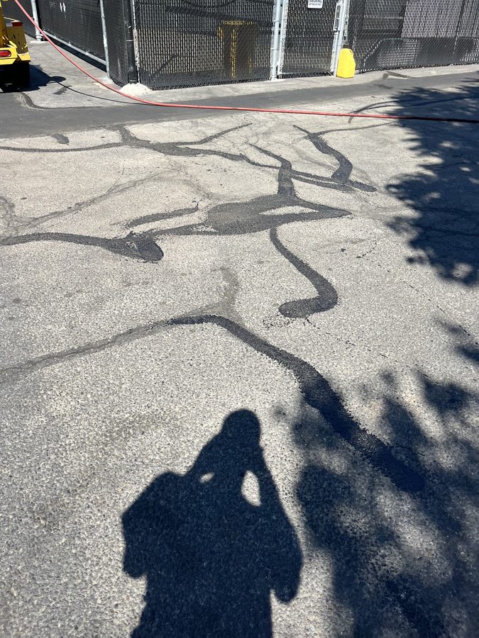 Close-up of rubberized crack filler sealing a web of cracks in gray asphalt on a commercial lot on Market Street in Medford, Oregon