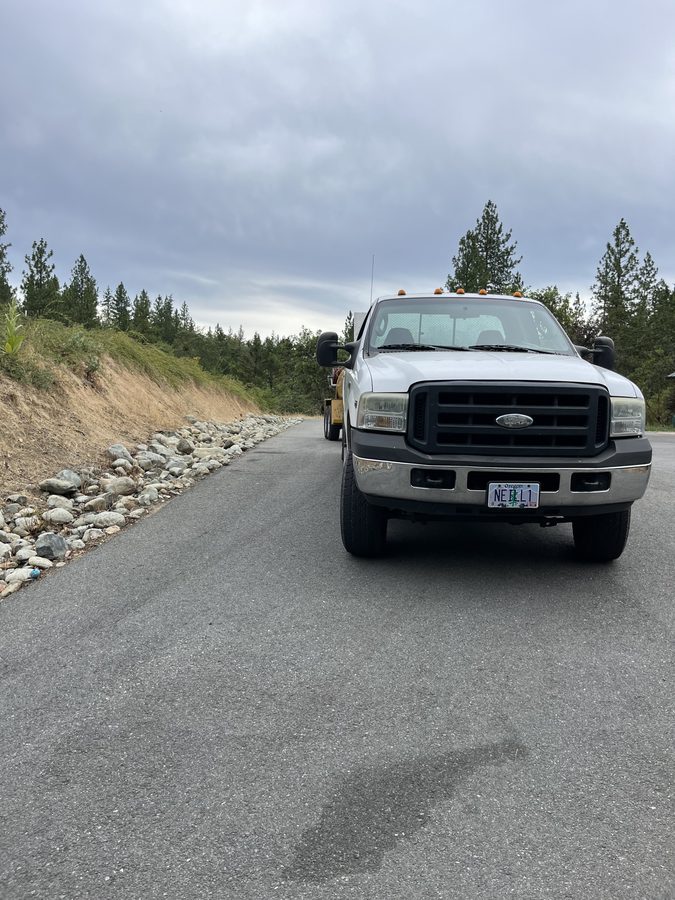 Pickup truck parked on a freshly sealcoated asphalt driveway beside a river-rock border on Seclusion Loop in Grants Pass, Oregon