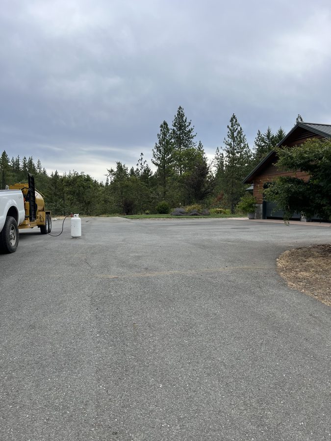 Wide freshly sealcoated asphalt driveway turnaround bordered by gravel and trees on Seclusion Loop in Grants Pass, Oregon