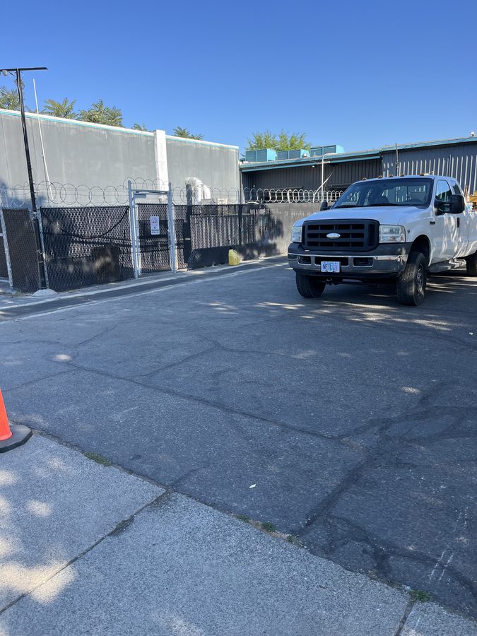 Cracked, weathered commercial parking lot with the Neill Sealcoating work truck on site before repairs on Market Street in Medford, Oregon
